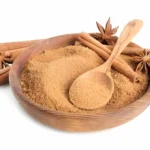 A bowl of cinnamon sticks next to a pile of granulated sugar