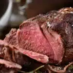 Perfectly cooked elk roast on a platter, garnished with herbs and ready to serve