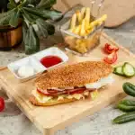 Close-up of a honey pepper pimento chicken sandwich on a wooden board, highlighting the juicy chicken, melting cheese, and vibrant toppings