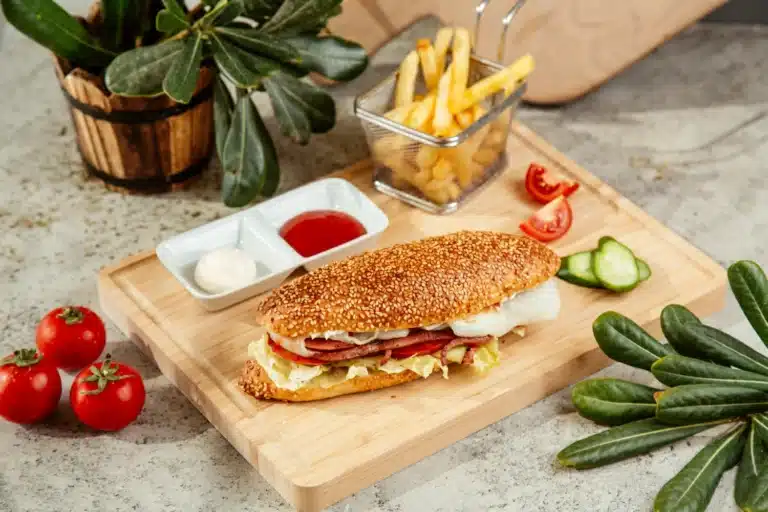 Close-up of a honey pepper pimento chicken sandwich on a wooden board, highlighting the juicy chicken, melting cheese, and vibrant toppings