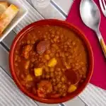 A bowl of hearty lentejas garnished with fresh parsley, served on a rustic wooden table, embodying traditional home-cooked warmth.